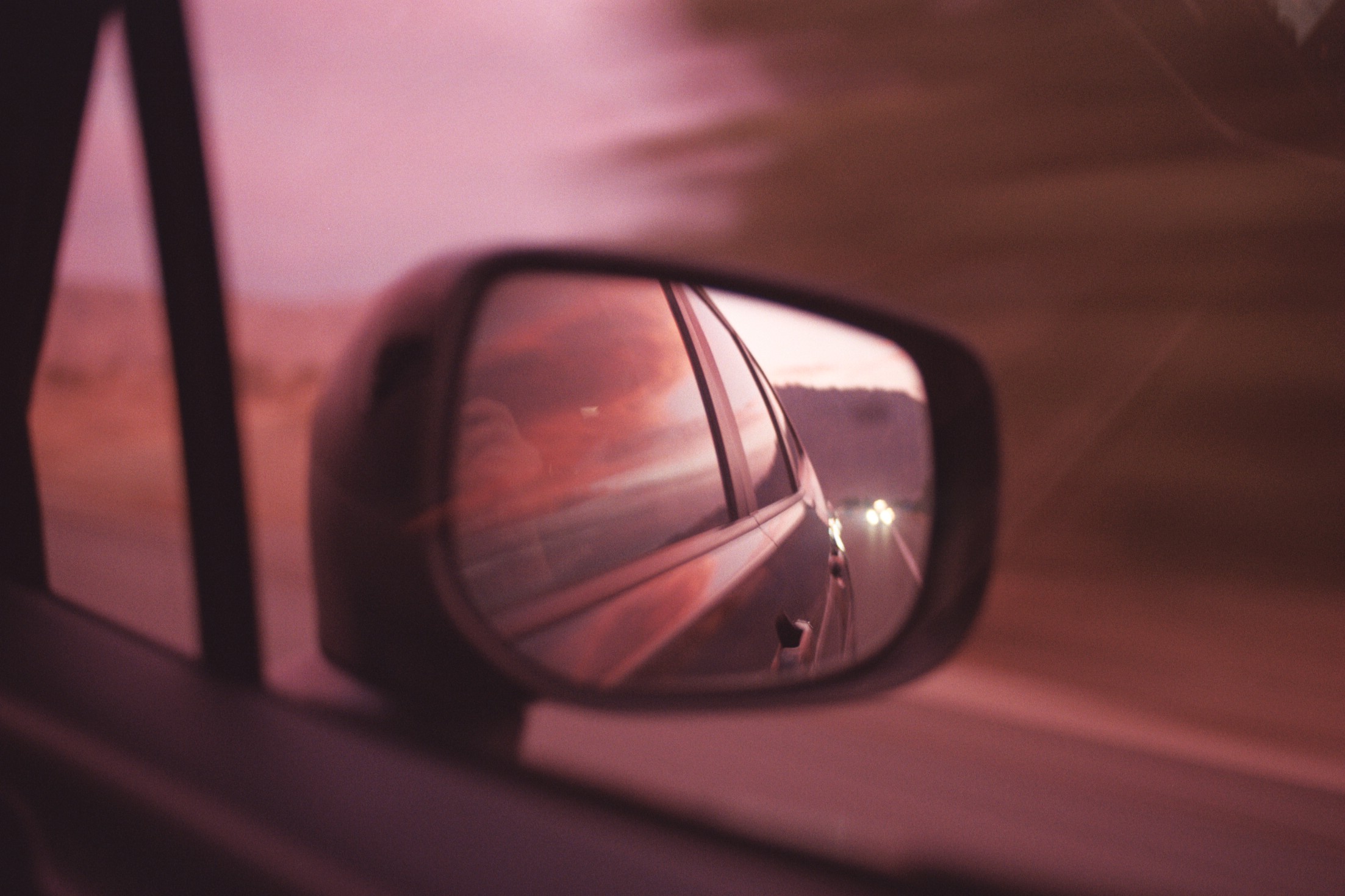 Sunset as seen in the side mirror of a car in the desert.