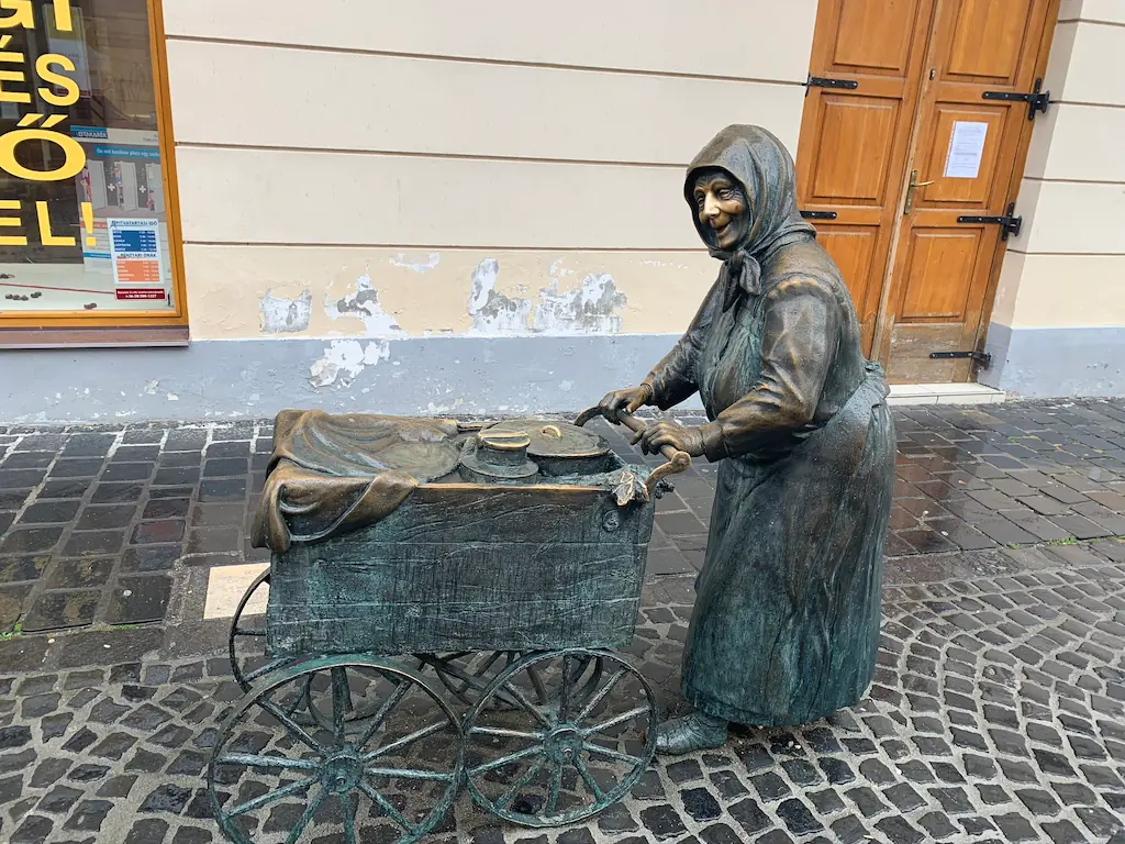 Bronze cast statue of an old woman pushing a cart